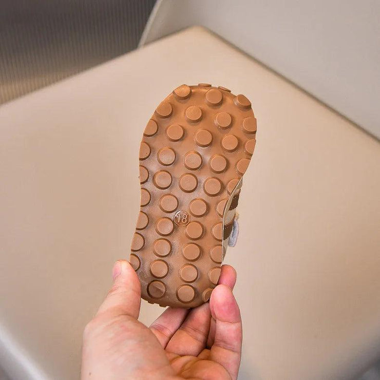 Close-up of a brown sneaker sole with a circular grip pattern, size 18 marking, and sturdy rubber material, held in hand.