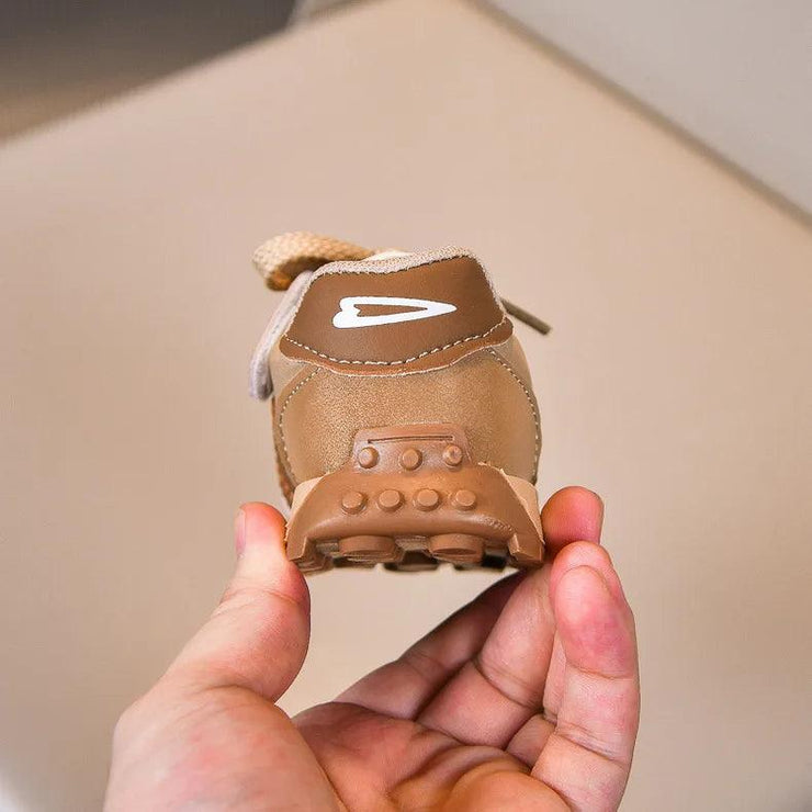 Brown and beige sneaker with a rugged sole, held in hand, showcasing the back logo.