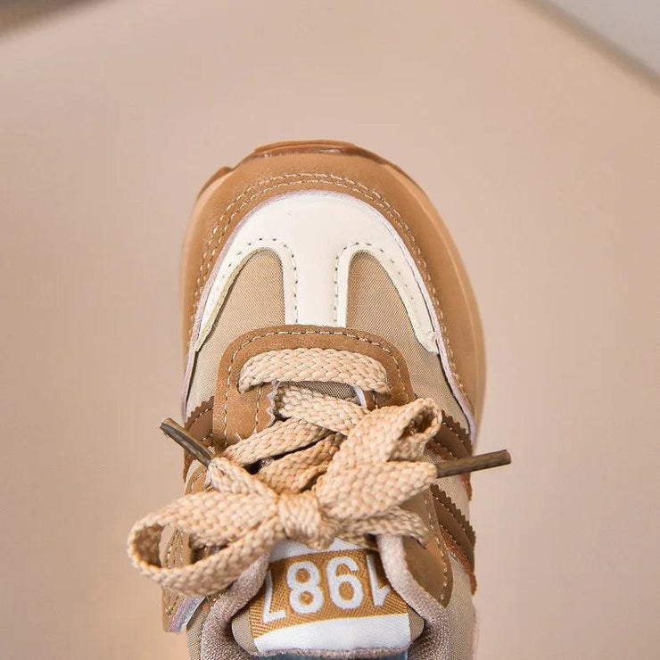 Close-up of a beige and white sneaker with “1987,” cream laces, and brown details.