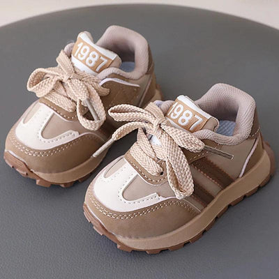 Beige and white toddler sneakers with “1987,” cream laces, and brown soles.