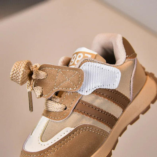 Brown and beige kids' sneaker with laces, Velcro strap, and “1987” on the tongue.